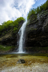 Fontanon of Goriuda, Udine. Wonderful waterfall that falls from a cliff. The force of the waterfall is a sight to behold. Hiking, trekking in the open area surrounded by woods. Summer holidays, peace.