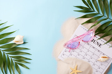 Flat lay featuring June calendar with beach accessories on a sandy background, suitable for articles about summer planning