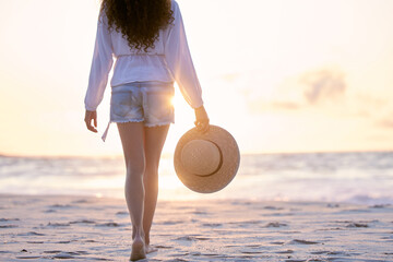 Beach, sunset and legs of woman walking on holiday, vacation or tropical summer travel outdoor in Hawaii. Back, ocean and feet at sea on sand in nature with hat for adventure, journey or mockup space © peopleimages.com
