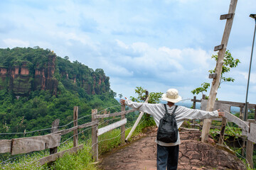 Hiker man with both arms extended and standing watching nature on beautiful rocky mountain and forest against morning sky for travel and hiking concept.