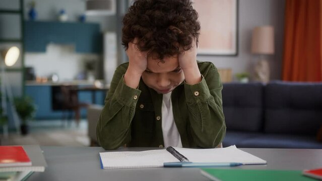 Sad upset little African American child adopted multiracial kid boy pupil schoolboy son health problem headache migraine pain holding head difficult task home education study learning trouble tired