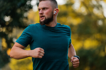 Sporty man running or jogging at the park listening to music on wireless headphones active healthy...