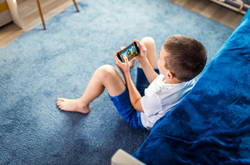 Boy playing video game on smartphone sitting on floor in his room.