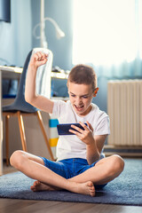 Boy playing video game on smartphone sitting on floor in his room.