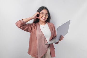 Cute young business Asian woman holding a laptop making finger heart shape over isolated white background.