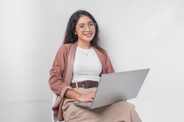 Smiling young Asian business woman sitting down and holding a laptop open over isolated white background.