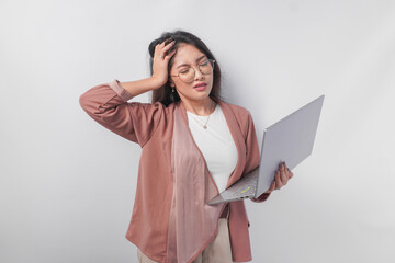 Overworked young Asian business woman holding a laptop hand on head feeling stressful, isolated by white background.