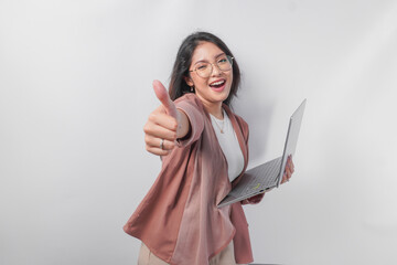Cheerful young Asian business woman showing thumbs up and holding laptop on isolated white background.