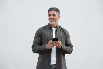Middle age handsome mature man in casual shirt holding smartphone cellphone and looking aside with...