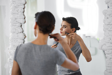 A young woman massages her face with gouache while looking in the mirror.