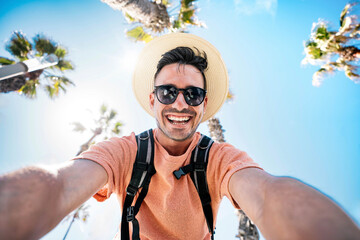 Happy tourist taking self portrait outside with cellphone on summer vacation - Handsome young man...