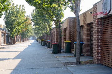 A row of garages of residential townhouses on the back street with some household rubbish bins placed on the roadside. Point Cook, Melbourne VIC Australia