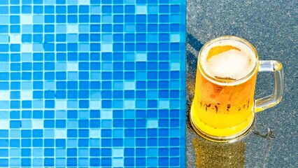 Frothy beer mug resting beside vibrant blue tiled swimming pool, embodying summer leisure trend...