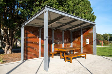 A picnic table is sitting under a covered shelter, which has a metal roof that extends outwards...