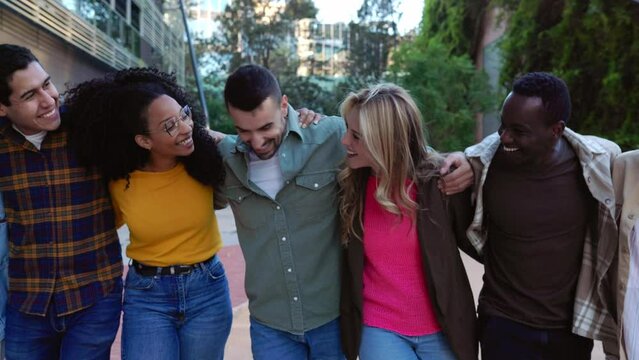 Happy young group of multiracial friends laughing while walking together at city street. Millennial people generation bonding enjoying time outdoors. Friendship lifestyle concept. Slow motion.