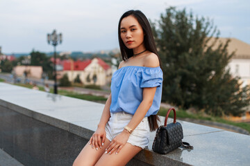 Fashion beauty Asian woman in summer clothes with top and shorts with leather bag sits on the street
