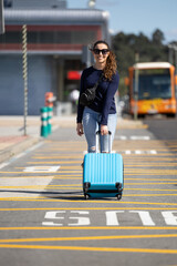 woman walking with her blue suitcase towards the airport to go on vacation