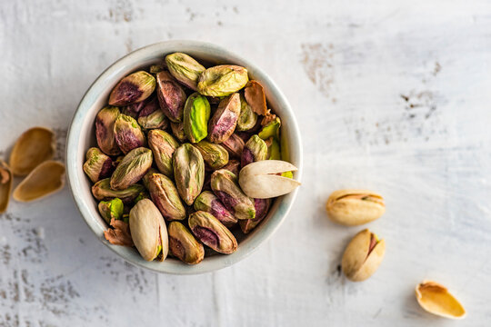 Ceramic bowl with organic pistaschio nuts on white wooden table background