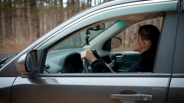 Woman carefully drive through rough terrain, attentively watching road in forest. Female learn driving and traveling alone. Shooting from outside