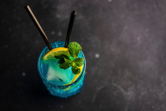 Cocktail high glass with blue kamikaze drink decorated with fresh mint and slice of lemon