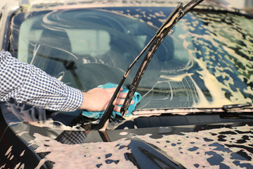 At a car wash, a man wipes foam from the windshield of a car (part of the series “at the car...