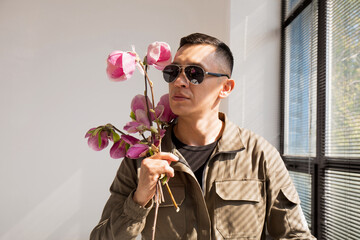 A man in sunglasses with a bouquet of magnolia near a window