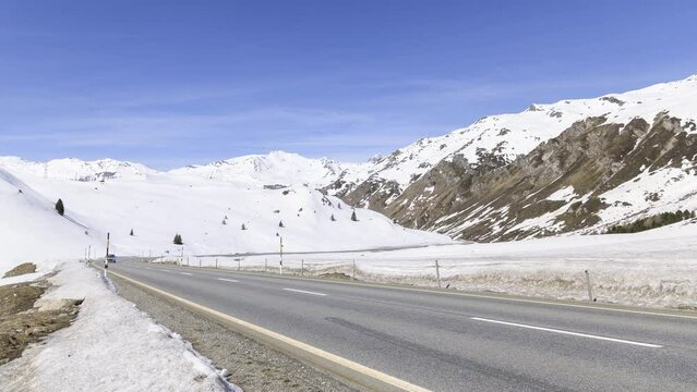 Passing traffic betweeen snowy slopes on Julier Pass in Switzerland on a sunny day - Time Lapse