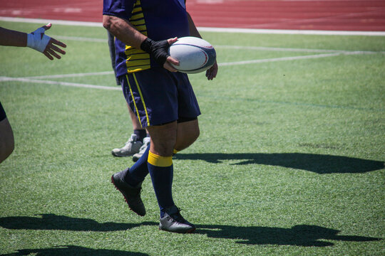 Group of men playing rugby on grass field, tackling and passing ball in action-packed match.