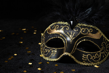 Close-up view of Masquerade gold mask with feathers and confetties on black background.