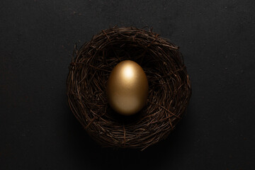 Gold egg in nest on black background. Easter concept.