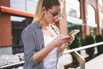 Concentrated young woman wear in trendy apparel messaging via smartphone with 4g connection in...