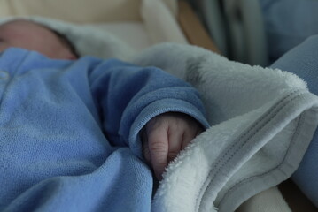 A detailed close-up of a newborn baby’s hand resting on a soft white blanket. The baby's tiny...