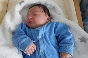 A serene newborn baby in a blue onesie, peacefully asleep in a soft white blanket, capturing the pure and innocent moments of early life with a hint of a smile.