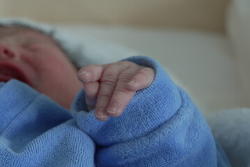 A close-up of a newborn baby’s hand, fingers gently curled, dressed in a blue onesie, highlighting the delicate and precious nature of a newborn’s first days.