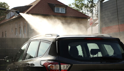The car is washed at a car wash with a high pressure washer (part of the “at the car wash”...