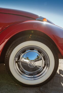 Red Beetle wheel . Tire with white stripe and chrome hubcap glowing in sunny day with blue sky.