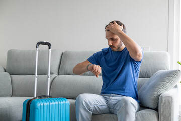 man looking the time with the hand on his head and his blue suitcase ready to go on vacation