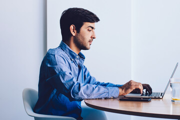 Serious indian male it professional typing program code at laptop device sitting at office table,...