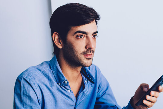 Young pondering man thoughtful looking away holding smartphone with 4g connection, concentrated male office worker in formal wear waiting for call via cellular, concept of technology and communication - Powered by Adobe
