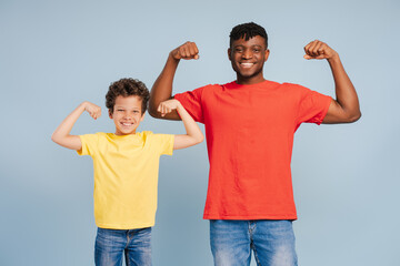 Smiling handsome African American man, father and little boy showing muscles, looking at camera
