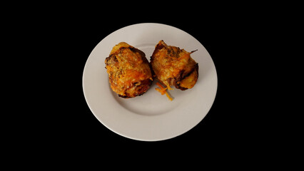
potatoes wrapped in bacon, sprinkled with cheese and baked. On a white plate on a black background.