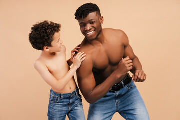 Happy African American father and little son with naked torso standing isolated on beige background