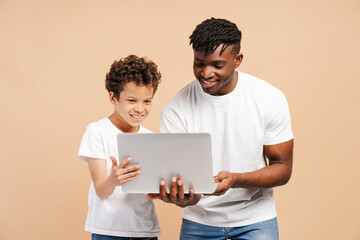 African American man, father and his little cute son, using laptop, watching video, playing game