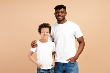 Attractive, young African American man, father and his little son wearing white t shirts hugging