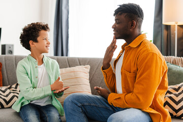 Happy, positive African American little boy and his dad communicating with sign language
