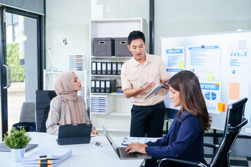 Comprehensive financial chart adorns the whiteboard during a presentation, where male and female business professionals, including a Muslim woman in hijab, engage in a productive meeting.