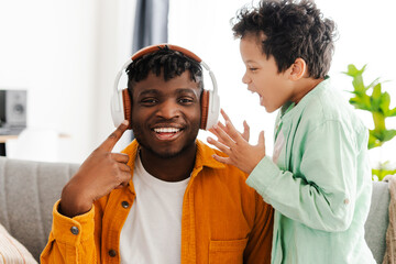 Smiling African American man listening to music in headphones, little boy, little son screaming