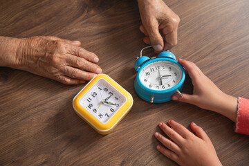 Hands of elderly female and young girl holding clock.