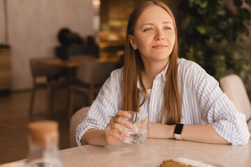 Delighted girl sitting in the cafe hold and drink glass of water resting in restaurant. Food,...