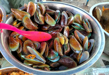 Selective focus. Mussels in spicy sauce on a stainless steel bowl on a wooden background horizontal. Yummy seafood.
